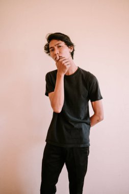 Düşünceli bir Güneydoğu Asyalı adam çenesini tutuyor, günlük giysiler içinde, dalgın dalgın uzaklara bakıyor, iç gözlem ve tefekkür anını yakalıyor..