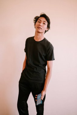 Ciddi bir ifadeyle Güneydoğu Asyalı bir adam, elleri cebinde, sakin ve düşünceli bir tavır sergiliyor.