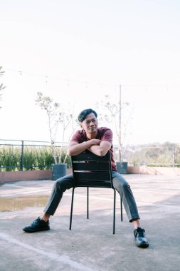 Güneydoğu Asyalı bir adam bir binanın balkonunda sandalyede oturuyor, manzaranın tadını çıkarıyor ya da dinleniyor. Boş zaman temaları, kentsel yaşam ve açık alanlar için mükemmel..