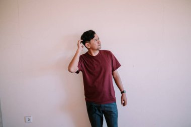 Güneydoğu Asyalı bir adam kafasını tutuyor, kafası karışmış ve kafası karışmış görünüyor. Şaşkınlık, sorun çözme ve duygusal ifade temaları için mükemmel..