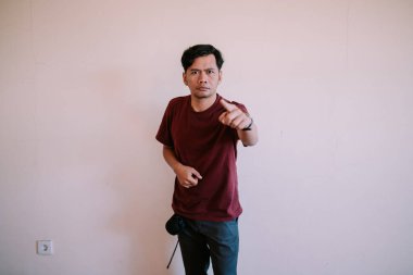 Güneydoğu Asyalı bir adam, odaklandığı ve kararlılığını ifade ederek, ciddi bir şekilde ileriyi işaret ediyor. Liderlik, yön ve özgüven temaları için ideal.