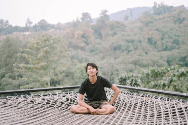 Güneydoğu Asyalı bir adam ağda dinleniyor, manzaralı bir manzarası var, doğanın ortasında huzurlu ve huzurlu bir anın tadını çıkarıyor.