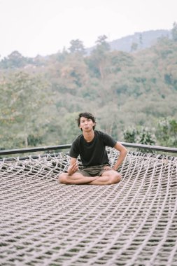 Güneydoğu Asyalı bir adam ağda dinleniyor, manzaralı bir manzarası var, doğanın ortasında huzurlu ve huzurlu bir anın tadını çıkarıyor.