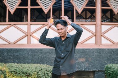 Güneydoğu Asyalı adam saçını tarıyor, aydınlık bir ortamda kendine çeki düzen veriyor.