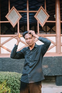 Güneydoğu Asyalı adam saçını tarıyor, aydınlık bir ortamda kendine çeki düzen veriyor.