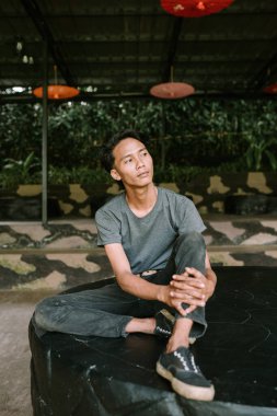 Güneydoğu Asyalı bir adam taş bir bankta oturuyor, ayaklarını yakınlardaki bir sandalyede dinlendiriyor, rahat ve rahat görünüyor.