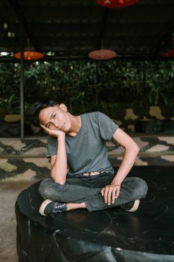 Güneydoğu Asyalı bir adam elini uzatıp arkasını yaslıyor, rahat görünüyor.