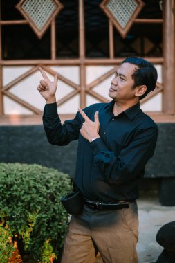 Düzgün giyinen Güneydoğu Asyalı adam sağına odaklanarak işaret ediyor. Yön temaları, liderlik veya kılavuz talimatlar için ideal.