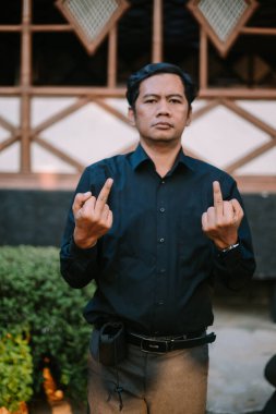 Güneydoğu Asyalı bir adam meydan okuyan bir ifadeyle orta parmağını gösteriyor. İsyan, öfke ya da güçlü duygular için uygun temalar