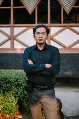Güneydoğu Asyalı adam kollarını kavuşturarak sakin ve kendinden emin bir duruş sergiliyor. Otorite, güven ya da düşünceli düşünce temaları için ideal..