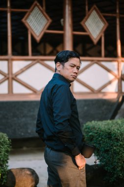 Güneydoğu Asyalı adam omuzunun üzerinden ileriye bakarken geriye doğru bakıyor, dinamik ve gizemli bir poz veriyor. Merakın, yansımanın ya da tarzın teması için ideal.