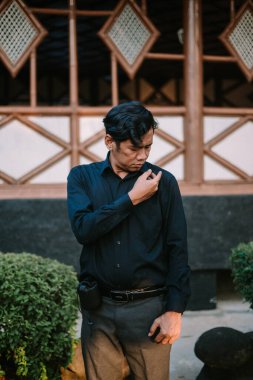 Gömleğinin tozunu alan Güneydoğu Asyalı adam, kıyafetlerini temizlemeye odaklanmış. Kişisel hijyen, temizlik ya da dış görünüş için mükemmel bir tema..