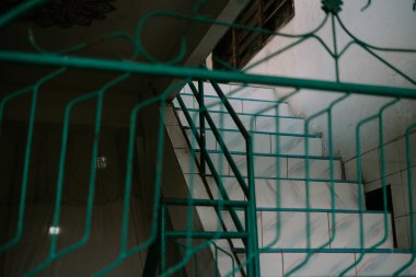 Yeşil korkuluklardan geçen merdiven manzarası derinlik ve entrika hissi katıyor..