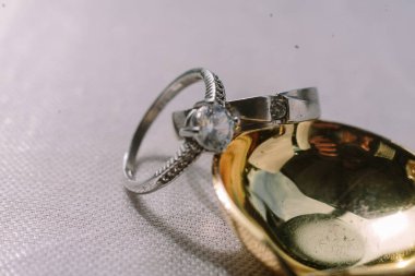 Parlak pırlanta bir alyans ve altın bir kaşığın yanında duran gümüş bir yüzük, değerli bir anın özünü yakalıyor..