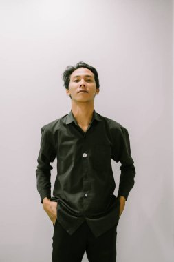 Siyah gömlek ve pantolon giymiş, minimalist bir geçmişe sahip, kendinden emin bir gencin portresi..