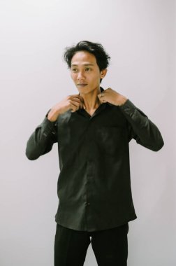 Yakasını siyah bir gömlekle düzelten adam, basit bir arka plan..