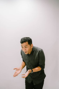 Şaşırmış bir adam, elleri açık ve şok olmuş bir ifadeyle beklenmedik haberlere tepki veriyor..