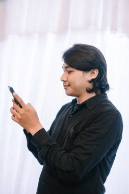 Genç bir adam akıllı telefonunu kullanır, muhtemelen bakınır ya da mesaj atar..