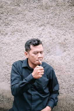 Bir adam dokulu bir duvara karşı sigara içiyor..