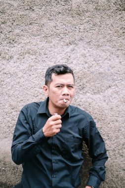 Bir adam dokulu bir duvara karşı sigara içiyor..