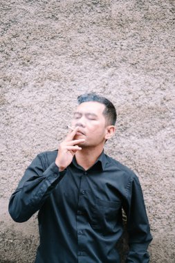 Bir adam dokulu bir duvara karşı sigara içiyor..