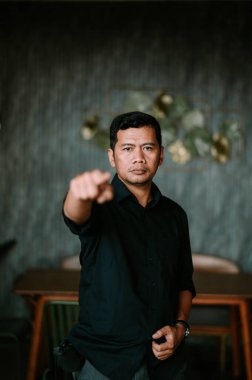 Koyu renk gömlekli bir adam ciddi bir ifadeyle doğrudan izleyiciyi işaret ediyor. Bu jest güven ve bir amaç taşımaktadır. Arkaplanda, güvenilirlik ve belirleyici bir acti mesajı iletmek için uygun çağdaş bir iç ortam sunuluyor.