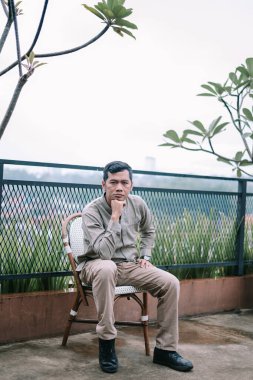 Düşünceli bir adam bir sandalyede oturmuş şehri gözlemlerken derin derin düşünüyor. Duruşunda düşünceli görünüyor, kentsel koşuşturma arasında bir huzur anı buluyor, düşüncelere ve içgözlem yeteneğine izin veriyor..