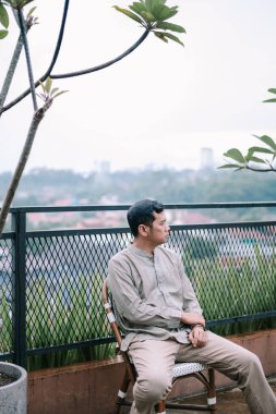 Düşünceli bir adam çatıdaki terasta güzel bir manzarası olan bir sandalyede dinleniyor. Sıradan giyinmiş ve derin düşüncelere dalmış gibi görünüyor. Şehir manzarasına tepeden bakan huzurlu bir anın tadını çıkarıyor. Huzurlu ve rahatlatıcı bir sahne..