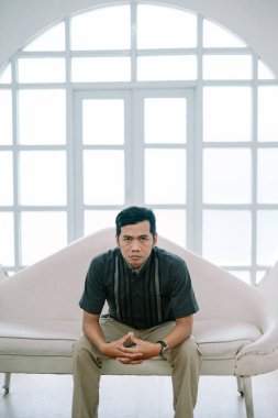 Zarif bir kanepede oturan Asyalı bir adamın portresi. Parlak pencereli. Kameraya bakıyorum. Tarz sahibi, düşünceli, güven ve sükunet dolu..