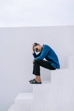 Gündelik giyinmiş genç bir adam beyaz basamaklarda oturur, elleri başının üstünde, düşüncelere dalmış. Minimalist mimari ve temiz çizgiler bu iç gözlem sahnesi için çağdaş bir ortam yaratır. Tarafsız zemin, deneğin duygusal durumunu vurgular..