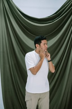 Düşüncelere dalmış, elleri yanağında dinlenen genç bir adam düşünceli bir davranış sergiliyor. Örtülü yeşil zemin bir derinlik katmanı ekliyor. Huzurlu ve içe dönük bir portre oluşturuyor..