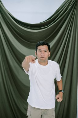 Ciddi bir ifadesi olan bir adam doğrudan izleyiciyi işaret ediyor. Kararlı ve odaklanmış görünüyor. Arka plan basit, jestine ve ifadesine dikkat çekiyor. Görüntü, aciliyet ve önem taşıyor..