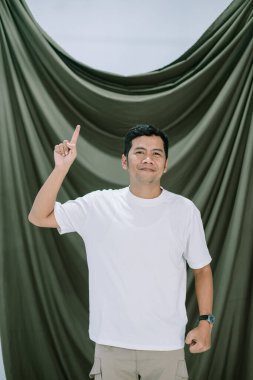 Gayri resmi beyaz gömlekli, tutkulu bir adam yeşil bir arka plana doğru parmağını yukarı kaldırarak emin bir şekilde işaret ediyor. İyi bir fikir veya çözümü temsil eden kavramsal bir görsel, iletişim, rehberlik ve motivasyonu gösterir.