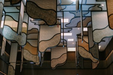 Katmanlar halinde asılı geometrik şekilli dalgalı paneller içeren mimari bir tavan kurulumu. Sanatsal tasarım modern bir iç mimari yaratıyor. Şık bir dekorasyon ve benzersiz, görsel olarak çarpıcı bir form. Çevre aydınlatması dokuları vurgular