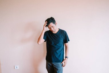 Koyu renk tişörtlü, stresli ve endişeli genç bir adam, endişe içinde başını kaşıyor. Depresyon, üzüntü ve derin kararlar. Kapalı alanda izole edilmiş..