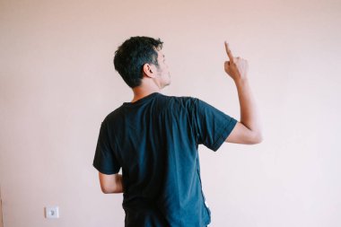 Adam sırtı kameraya dönük duruyor ve parmağını düz bir duvara doğrultuyor. Bu resim fikirler, kavram, yön, öneri, sunum, çözüm, ilham veya cevap arayışı için uygundur