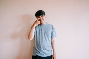 Düşünceli Asyalı bir adam düz bir duvara yaslanmış, parmağı hafifçe burnuna dokunuyor. Sıradan bir tişört giydiği için suratı dalgın, derin düşünmeyi ya da içgözlem yapmayı öneriyor. İlgili kavramları resmetmek için mükemmel