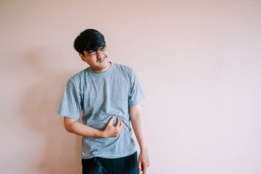 Şiddetli karın ağrısı çeken Asyalı bir adam. Rahatsızlık içinde yüzünü buruşturuyor ve karnını tutuyor. Hazımsızlık, gıda zehirlenmesi, mide krampları ya da diğer sindirim sorunları yüzünden olabilir. Görüntü fiziksel ifadenin altını çizer