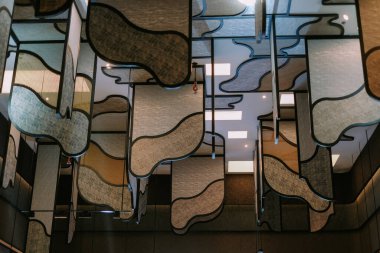 Katmanlar halinde asılı geometrik şekilli dalgalı paneller içeren mimari bir tavan kurulumu. Sanatsal tasarım modern bir iç mimari yaratıyor. Şık bir dekorasyon ve benzersiz, görsel olarak çarpıcı bir form. Çevre aydınlatması dokuları vurgular