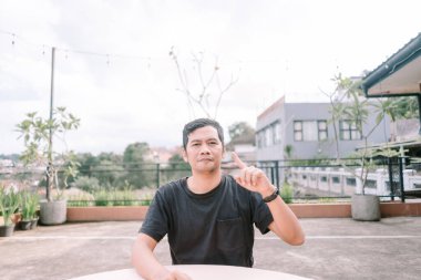 Terasta oturan düşünceli bir adam arka planda şehir manzarası olan bir fikri varmış gibi parmağını yukarı kaldırır. İlham, çözüm ve yaratıcılık kavramını gösterir