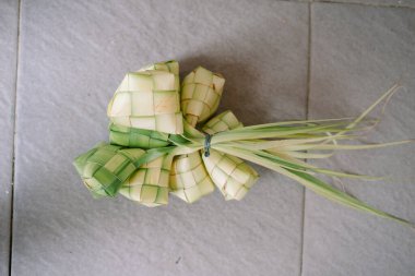 Bir grup ketupat, örülmüş palmiye yapraklarından yapılan geleneksel pirinç hamuru, tarafsız bir yüzeye karşı oturur. Bu bayram yemekleri genellikle Güneydoğu Asya 'da Kurban Bayramı sırasında yenir. Görüntü eşsiz dokuma desenini ve taze yeşil renkleri sergiliyor.