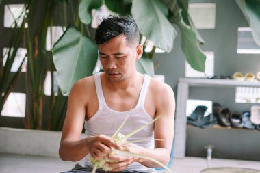 Bir adam şenlik vesilesiyle geleneksel pirinç köftesi olan ketupayı ustaca dokuyor. Bu aşçılık sanatı, Güneydoğu Asya 'nın zengin geleneklerini ön plana çıkaran, kültürel bir temel oluşturma sürecini gözler önüne seriyor..