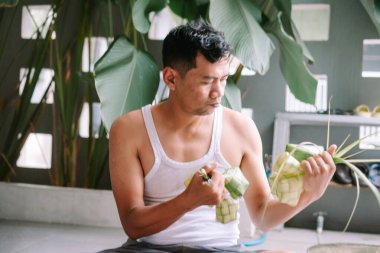 Asyalı bir adam ustalıkla ketupa işliyor. Geleneksel bir pirinç köftesi. Kültürel bir kutlamaya hazırlanıyor. Bu yerel aşçılık geleneği için gereken eşsiz sanat ve uzmanlığı gösteriyor..