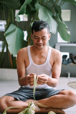 Bayram için ketupat hazırlayan adam, yerde oturuyor. Ketupat, hindistan cevizi yapraklarından örülmüş geleneksel bir pirinç hamurudur. Ketupat kaplamasını ustalıkla dokumak nesilden nesile geçen bir gelenektir. Bu bayram yemeği...