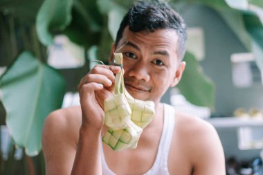 Kurban Bayramı 'nda dokunmuş palmiye yapraklarıyla yapılan geleneksel bir Endonezya pirinç yemeği olan Ketupat' ı elinde tutan bir adam. Güneydoğu Asya 'da kültür mirası ve festival geleneklerinin sembolü.