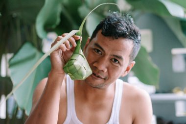 Bir portre, bayram kutlamaları sırasında elinde geleneksel pirinç köftesi olan ketupat tutan bir adamı yakalıyor. Kültürel mirası ve şenlikleri simgeleyen bu resim, aşçılık gelenekleri ve neşeli toplantıları resmediyor..