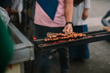 Satay 'ın, bir sokak yemeği standında kömür üstünde ızgara yaptığı yakın çekim. Bu lezzetli tavuk şişleri popüler bir Güneydoğu Asya lezzeti. Sokak satıcısı Asya mutfağı hazırlıyor. Dumanlı bir barbeküde pişirilen Endonezya yemekleri.