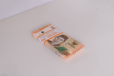 Birbirine bağlı bir yığın Endonezya Rupiah banknotu. Turuncu renkli para birimi beyaz bir yüzey üzerinde duruyor. Finans, zenginlik ve Endonezya ekonomisinin temsilcisi.