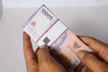 On bin Endonezya Rupia banknotundan oluşan bir yığını parlak bir arkaplanda tutan birinin yakın plan çekimi. Endonezya 'daki finans, ekonomi ve iş bağlamlarını resmediyor. Zenginliği, yatırımı veya ödemeleri temsil edebilir.