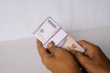 Endonezya Rupia banknotları tutan birinin yakın plan fotoğrafı. Resim, 10000 banknotun detaylarına odaklanır. Finansal kavramların, Endonezya ekonomisinin ve iş temalarının resmedilmesi için uygun.